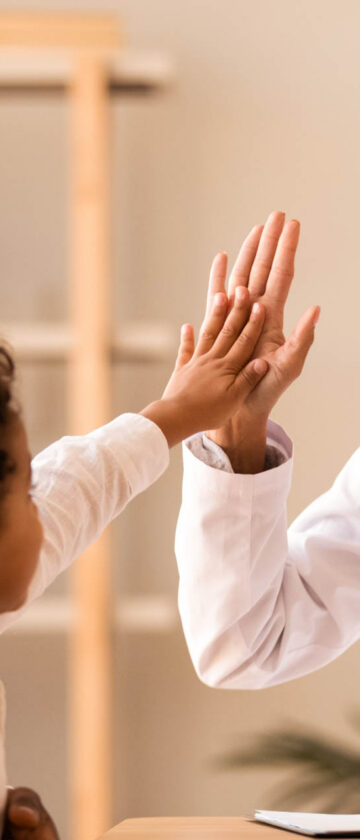 Læge giver high-five til barn under konsultation