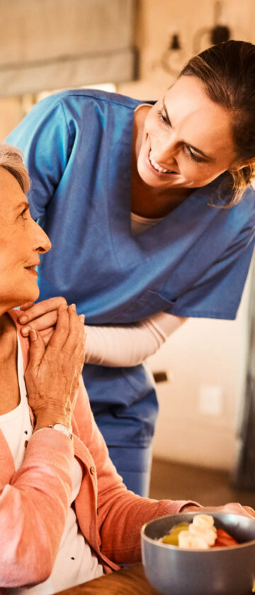Caregiver providing elderly woman with breakfast